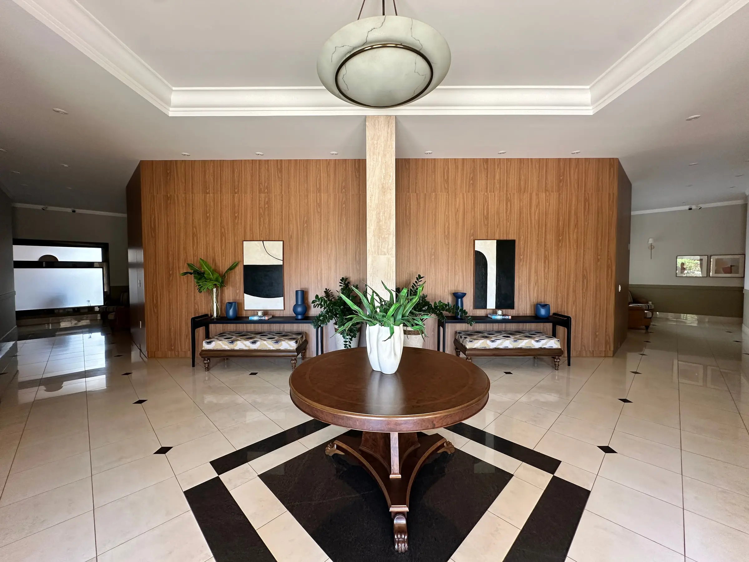 Hall social do condomínio no Jardim Irajá, com piso em mármore, painel de madeira e mesa central